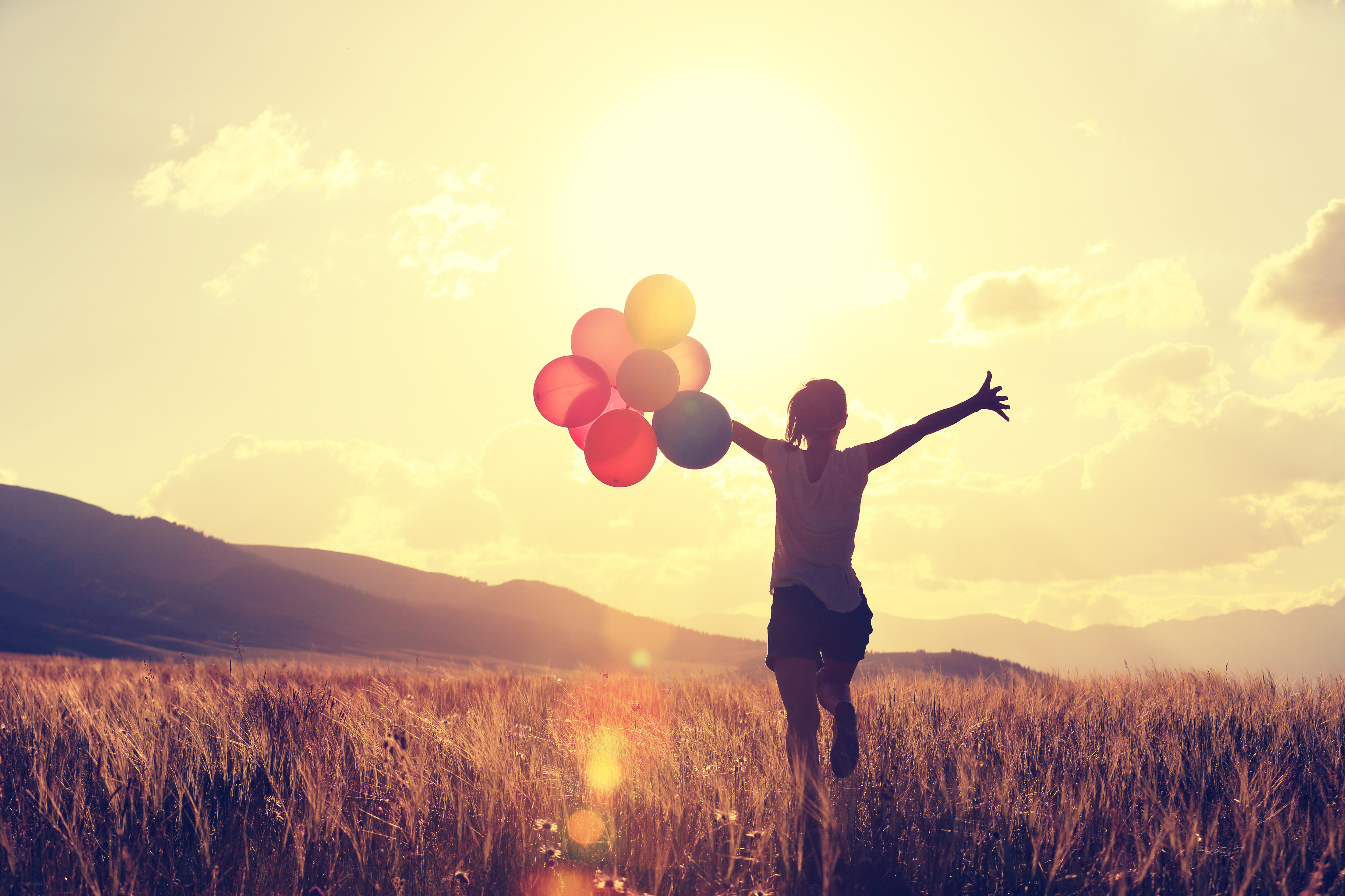 cheering young asian woman on grassland with colored balloons