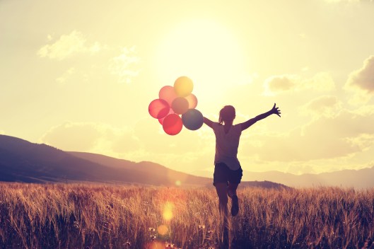 cheering young asian woman on grassland with colored balloons